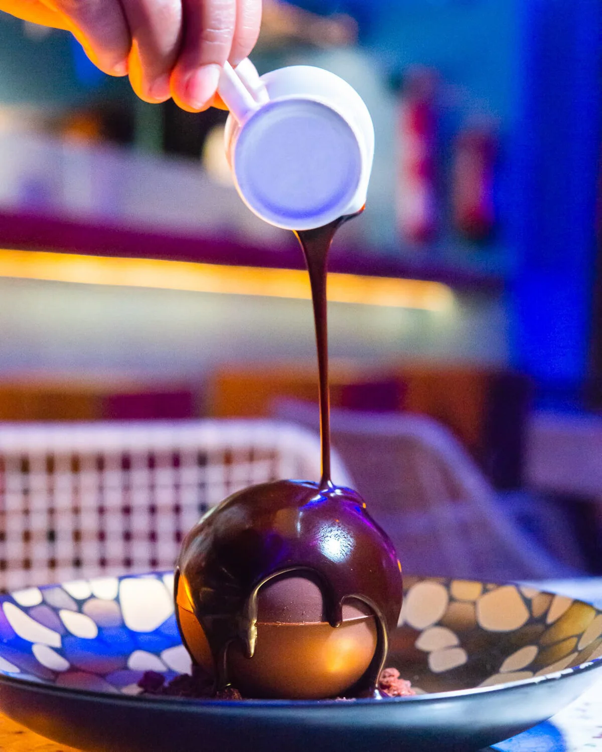 Chocolate sauce poured over a chocolate sphere dessert.