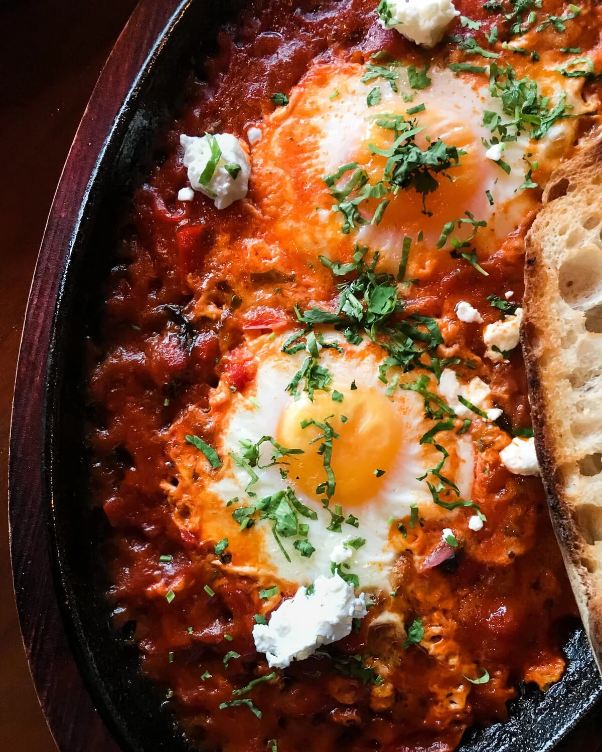 Shakshuka with eggs, herbs and toast in a dark pan.
