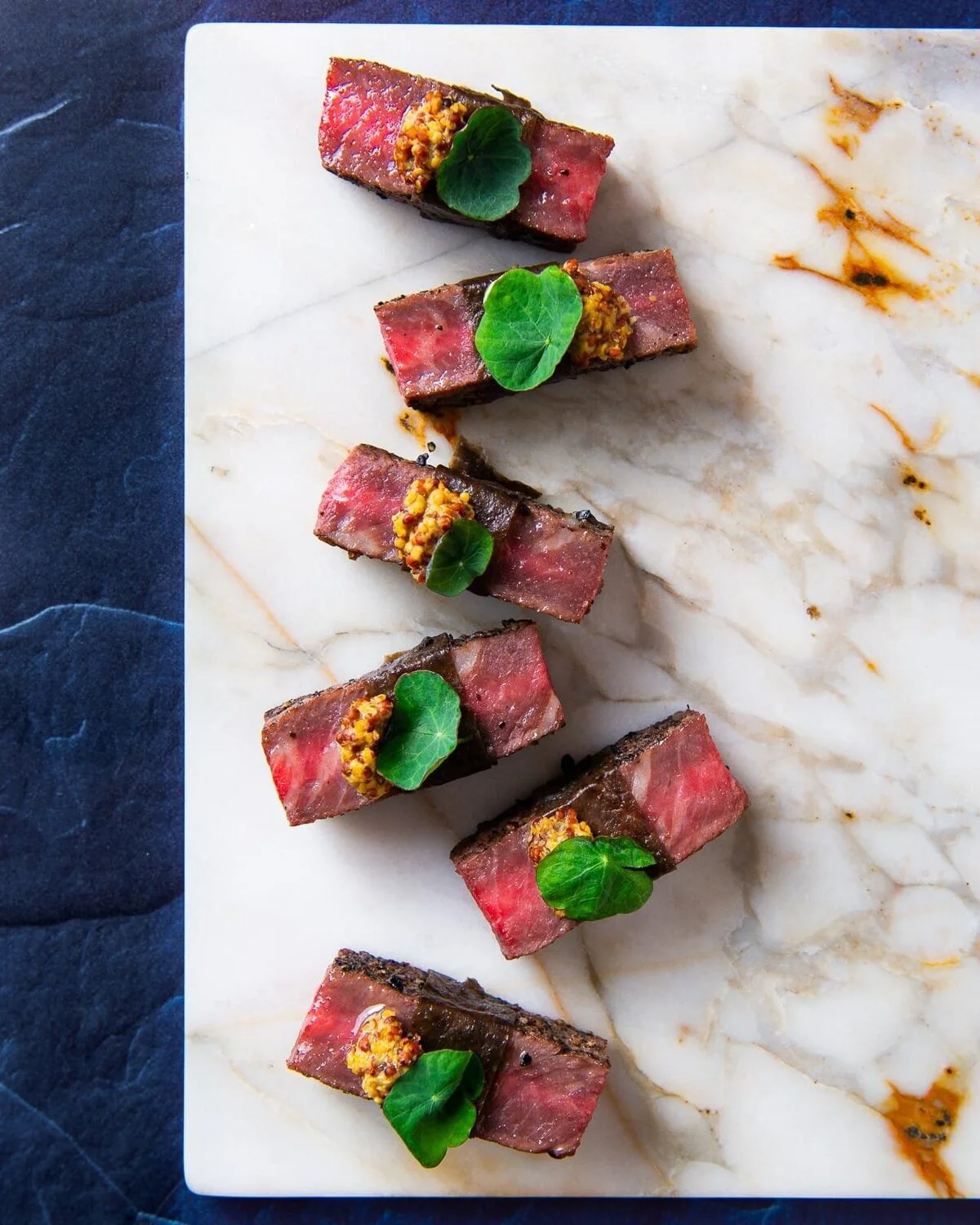 Bite-sized portions topped with green leaves on a pale marble slab.