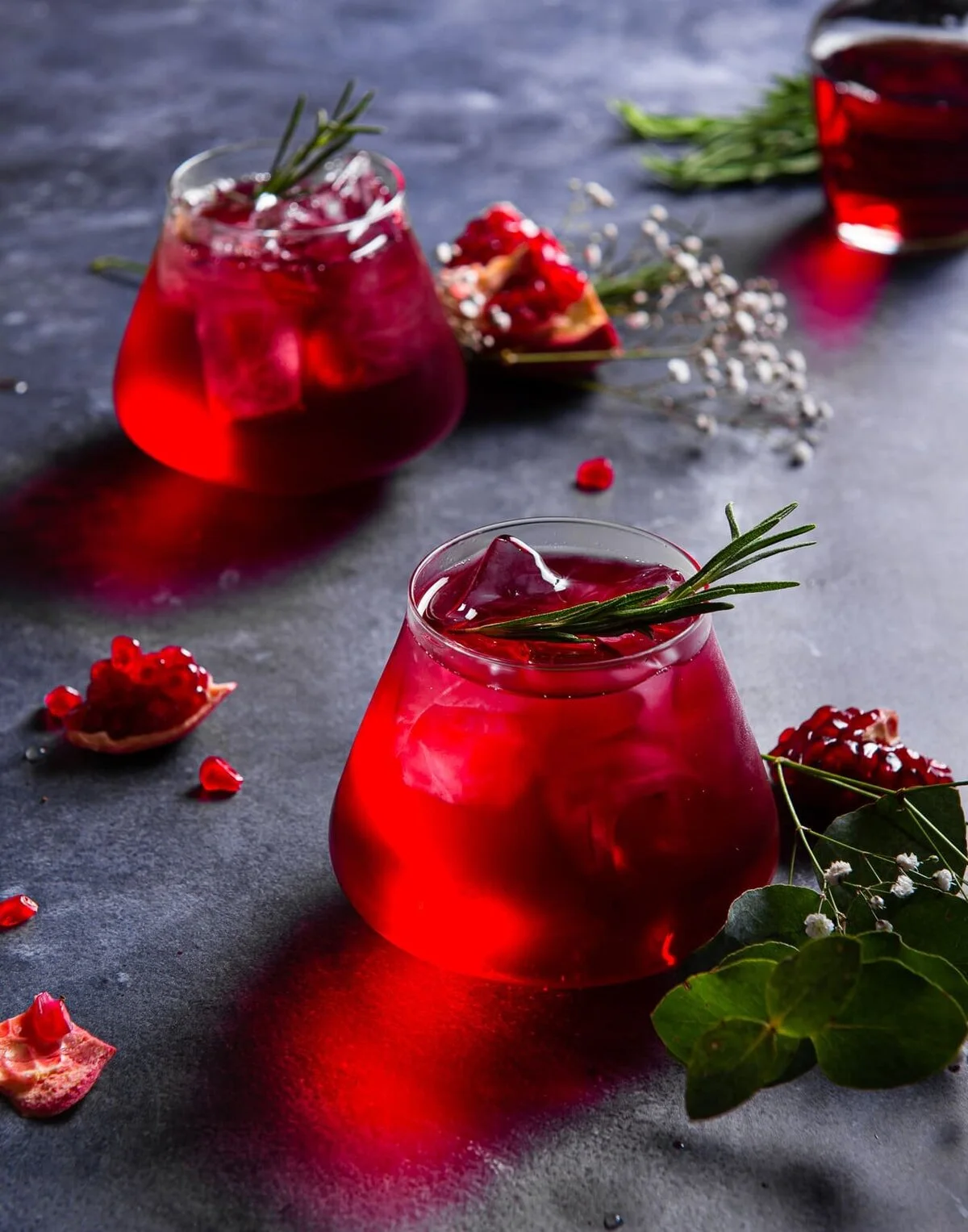 Crimson granita drinks with rosemary and pomegranate on dark slate.