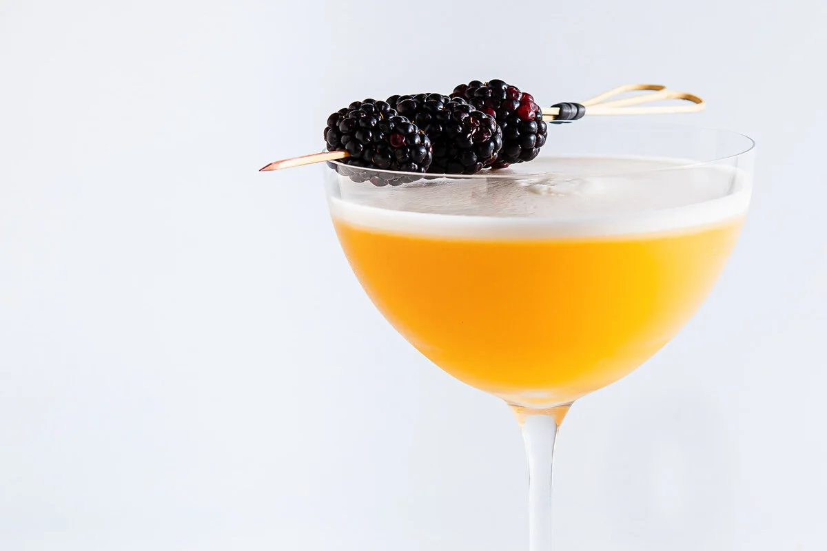 Golden cocktail in a coupe glass topped with dark berries.