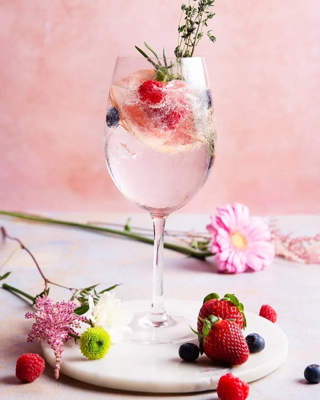 Pink drinks surrounded by berries and flowers.