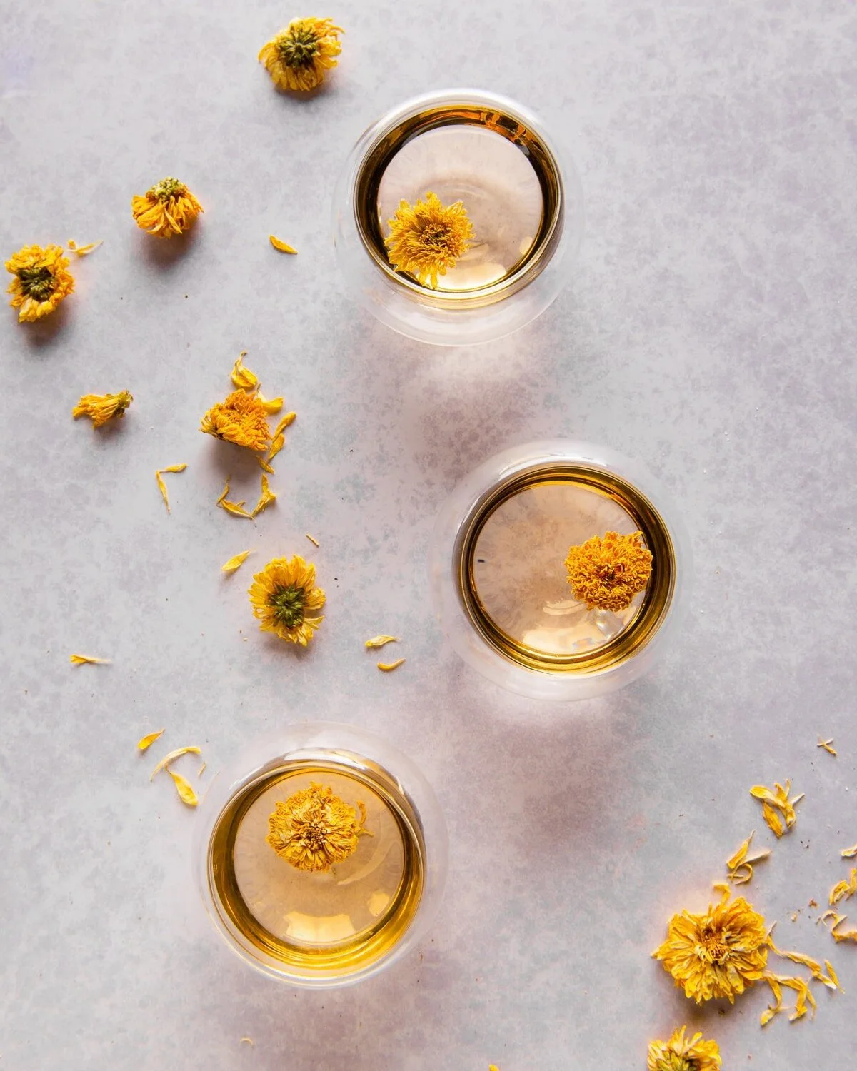 Glasses of flowering tea surrounded by dried flowers.