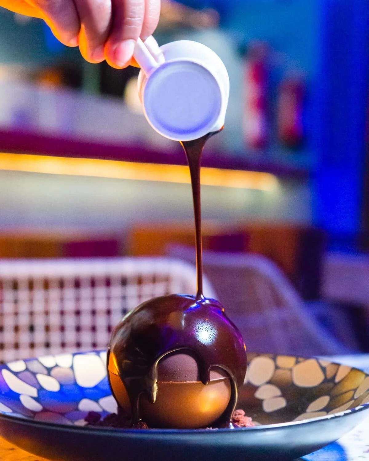 Chocolate sauce poured over a chocolate sphere dessert.